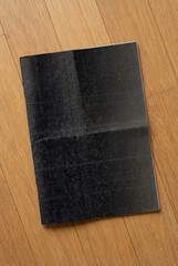 Minimalist magazine mockup with no cover, featuring subtle print lines and a worn paper texture. The blank black magazine lies on a wooden floor.