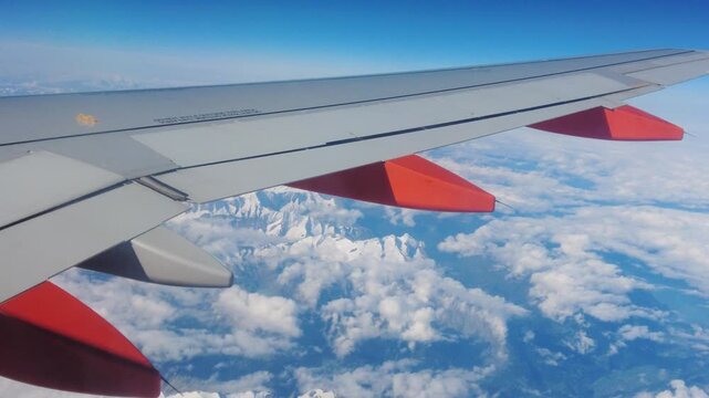 frames wing plane air thick clouds below snow capped mountains forming depth to revealing closeup top down view airplane peaks upward perspective altitude structure flight 