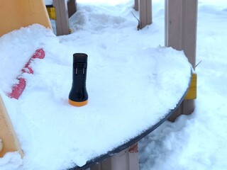 Black flashlight with yellow base standing on a snow-covered outdoor table. Winter season object outdoors. Equipment for dark.