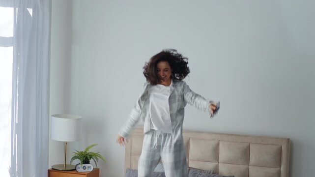 Happy excited Caucasian woman jumping on bed holding mobile phone celebrating winning victory celebrate good news female in bedroom jump with smartphone bet win winner girl having fun fooling around
