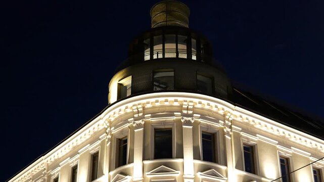 brightly illuminated neoclassical facade tall pilasters arched windows dark domed turret rises against deep blue sky historic building oslo norway architecture landmark nighttime lighting 