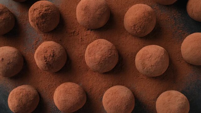 Chocolate truffles dusted with cocoa powder on a dark brown surface viewed from directly above