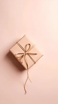 Square gift box wrapped with simple brown twine tied in bow on soft neutral pastel pink background in minimalistic style for celebration concept