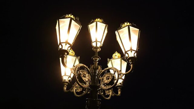 ornate multi headed streetlamp glows warmly decorative metalwork glass lanterns elegant clearly illuminated against deep black night sky oslo norway nighttime lighting infrastructure 