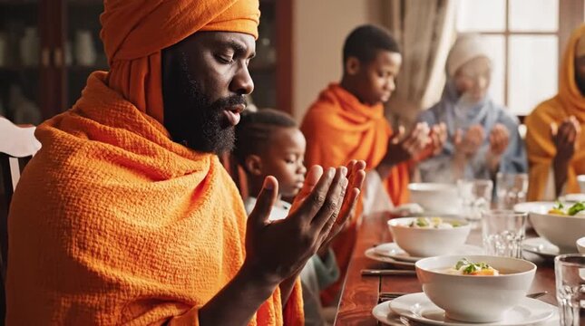 African Family in Traditional Orange Attire Praying Before a Meal, Hands Clasped in Gratitude at a Dining Table