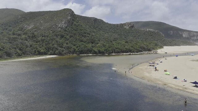 Drone flies across Groot River and up the hill on a sunny day in Nature's Valley, South Africa