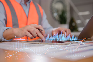 Engineer wearing safety vest using computer and digital tablet analysing data charts, Industrial engineer working on computer in factory control room, monitoring production process