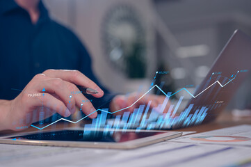 Businessman using computer laptop and digital tablet working in home office with virtual data charts in concept of business marketing and plans