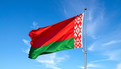 Belarusian flag waving on flagpole against blue sky with wispy clouds, national symbol with ornamental pattern