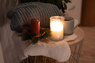 Cozy winter scene featuring a knitted blanket, candles, and a warm beverage on a wooden table, creating a serene atmosphere for relaxation and holiday comfort