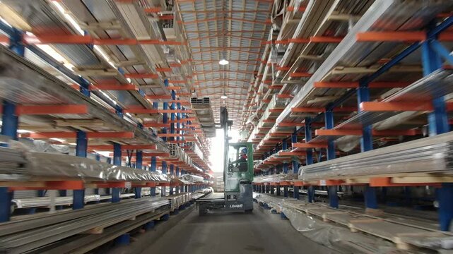 Drone moving away from forklift inside metal warehouse
