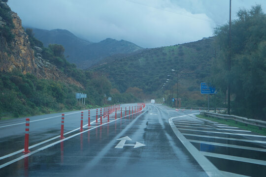 Rainy BOAK highway junction towards Rethymno, featuring white chevron markings and road signs for Fodele and Achlada villages under misty mountains and wet conditions.