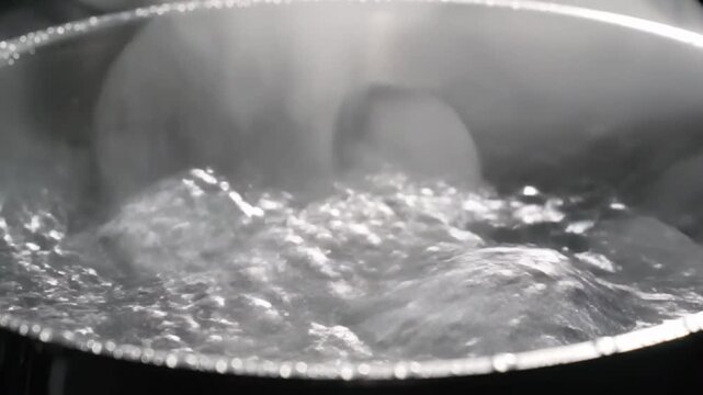 Close up of boiling water in a metal pot with rising steam