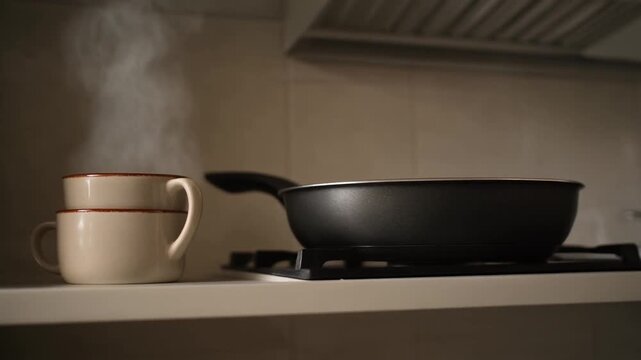 Steam rises from a stack of cups beside a pan on a kitchen counter