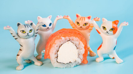 Funny plastic toy kittens dancing around a fresh salmon sushi roll with cream cheese. Concept of joy and food delivery on blue background. Photo