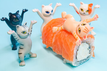 Funny plastic toy kittens dancing around delicious salmon sushi rolls. One cat is lying on top of the food. Concept of joy and sushi ordering on blue background. Photo