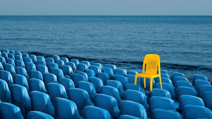 A vibrant yellow chair contrasts with a sea of blue seating overlooking a calm ocean expanse. The lone chair highlights difference