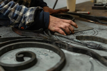Gros plan sur les mains d’un artisan ferronnier en atelier travaillant des pièces métalliques...