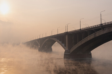 Naklejka premium Misty urban mystical landscape - an arched bridge over the Yenisei River on a foggy winter evening. The symbol of Krasnoyarsk. High quality photo