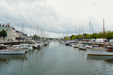 Beautiful view of the Port de Vannes in Brittany, France. Numerous sailboats and yachts are moored along the historic urban canal under a dramatic cloudy sky in this tourist destination