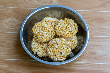 Traditional Murir Moa or Puffed Rice Balls in a stainless steel bowl. Crunchy Bengali sweet snacks made with jaggery, served on a wooden surface. Popularly known as Puffed Rice Laddoo or Cakes.