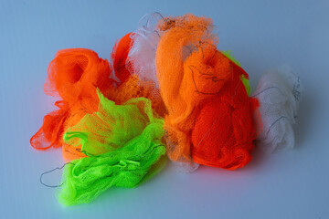 A messy pile of bright neon orange, green, and white nylon net bags on a gray background. Vibrant synthetic mesh texture, perfect for concepts of waste, recycling, or industrial plastic.