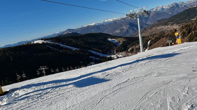 Following a skier carving on wide groomed slope in Folgaria ski resort, Italian Alps winter sports action. Skier carving on white slope during sunny winter day in Folgaria, Italian Alps ski resort wit