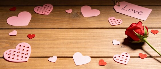 Wooden table background with red rose and paper hearts frame border, rustic Valentine's Day texture with central copy space for message