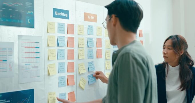 Group of Asian businesspeople work together collaborating and sharing ideas use colorful note on wall in business meeting in office. Financial generation z team brainstorm on e-Commerce project.