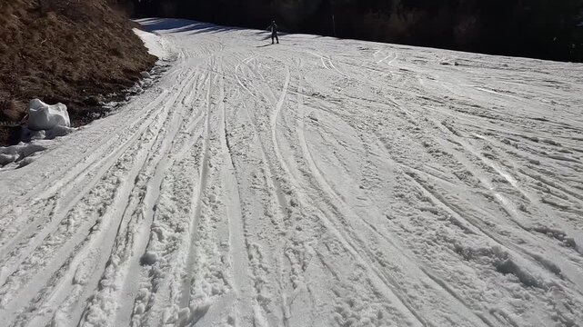 Following a skier carving on wide groomed slope in Folgaria ski resort, Italian Alps winter sports action. Skier carving on white slope during sunny winter day in Folgaria, Italian Alps ski resort wit
