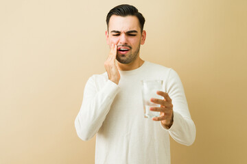 Man experiencing acute tooth sensitivity and dental pain from cold water, grimacing and touching...