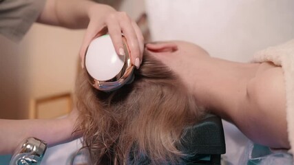 Japanese head spa treatment. A cosmetologist gives a head massage to a client using a massager in a spa salon. Young woman enjoying a spa treatment.