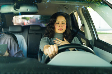 Anxious adult woman feeling stressed while driving, taking deep breaths and closing her eyes during a driving lesson