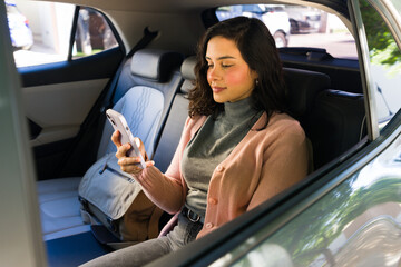 Young woman using rideshare mobile app inside car, checking phone while commuting comfortably during urban travel