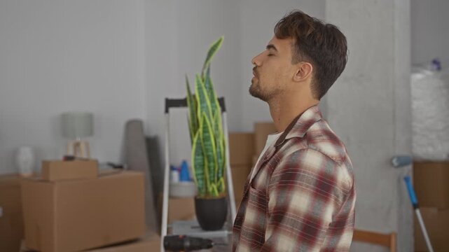 Young man relaxing in new home filled with boxes, plant, and ladder, symbolizing the start of a new chapter and the excitement of moving to a fresh living space.