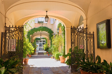 Through an archway leading to a courtyard in Rimini. Potted plants line the path, adding greenery to the setting. The area is quiet and inviting for exploration. Rimini, Emilia-Romagna, Italy