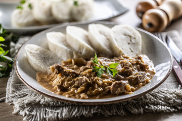Traditional Szeged goulash with pieces of meat and sauerkraut is served on a plate, complemented by a few slices of light steamed dumplings and garnished with parsley