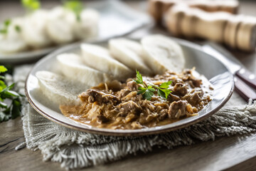 Traditional Szeged goulash with pieces of meat and sauerkraut is served on a plate, complemented by a few slices of light steamed dumplings and garnished with parsley