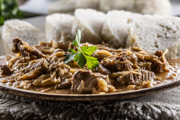 Traditional Szeged goulash with pieces of meat and sauerkraut is served on a plate, complemented by a few slices of light steamed dumplings and garnished with parsley