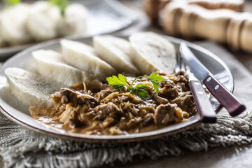 Traditional Szeged goulash with pieces of meat and sauerkraut is served on a plate, complemented by a few slices of light steamed dumplings and garnished with parsley