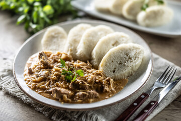 Traditional Szeged goulash with pieces of meat and sauerkraut is served on a plate, complemented by a few slices of light steamed dumplings and garnished with parsley