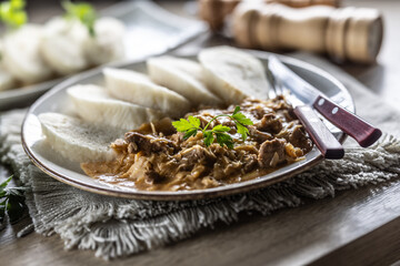 Traditional Szeged goulash with pieces of meat and sauerkraut is served on a plate, complemented by a few slices of light steamed dumplings and garnished with parsley