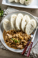 Traditional Szeged goulash with pieces of meat and sauerkraut is served on a plate, complemented by a few slices of light steamed dumplings and garnished with parsley