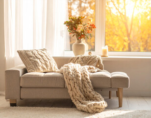 Cozy living room interior with chunky knit blanket on a fabric sofa in warm morning light