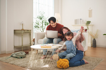 Asian family spending time together on the floor while using a laptop at home. Relaxed family lifestyle scene showing bonding, parenting, and shared activity.