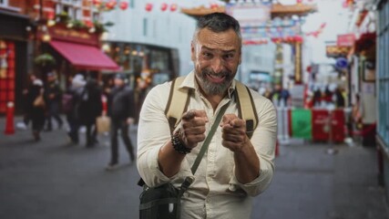 Man pointing index fingers at camera with backpack on busy street marketplace; playful travel discovery.