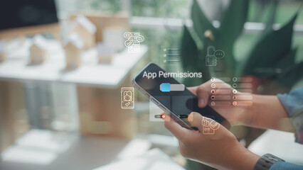 A person using a smartphone to manage app permissions and privacy settings with digital interface icons, focusing on data security and mobile protection in a home office setting.