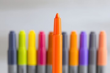 Bright orange marker stands prominently in front of a colorful array of vibrant markers, showcasing a creative workspace filled with artistic potential and inspiration