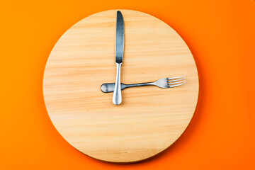 The concept of intermittent fasting and skipping meals. Wooden round tray with cutlery in the form of clock hands