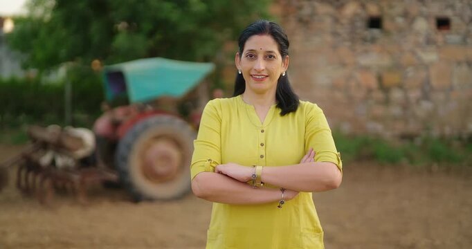 Indian gen x adult villager woman lady fold hand look camera standing outdoor rural area. Elder female staff officer do field visit work cross arm staring cam casual pose enjoy new day ground place